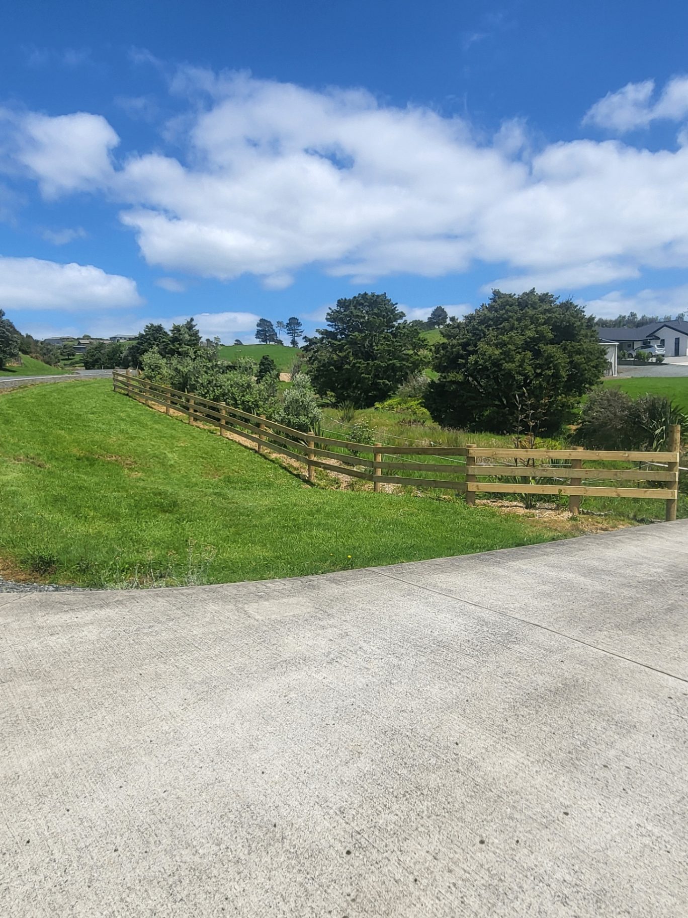 Completed rural post and rail fence beside a concrete driveway